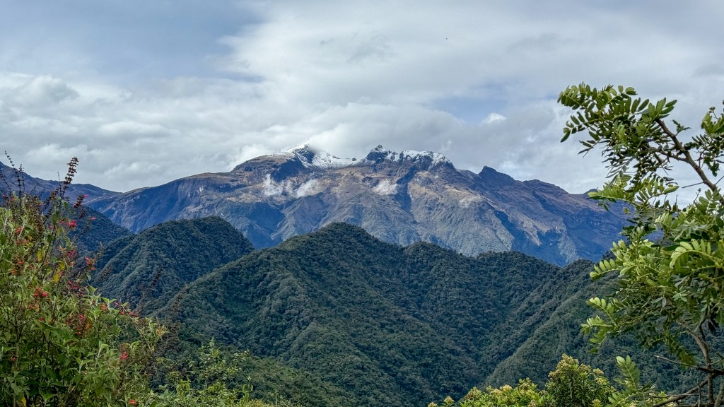Scenic view of snow-capped mountains and lush green hills under a cloudy sky.