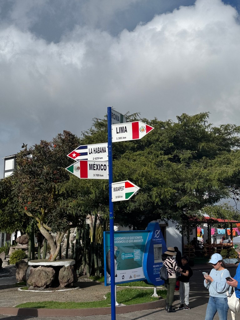Signpost indicating distances to various cities including Lima, La Habana, Mexico, and Budapest, surrounded by trees and a cloudy sky.